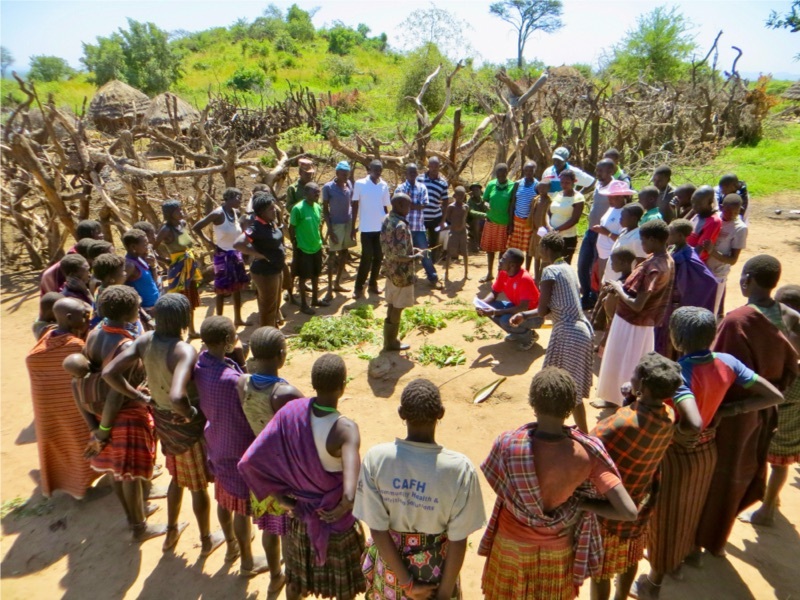 People standing in circle outside with instructor in the middle during a meeting.
