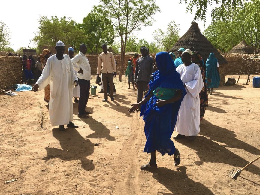 Group of people talking in refugee settlement, pointing at barren soil.