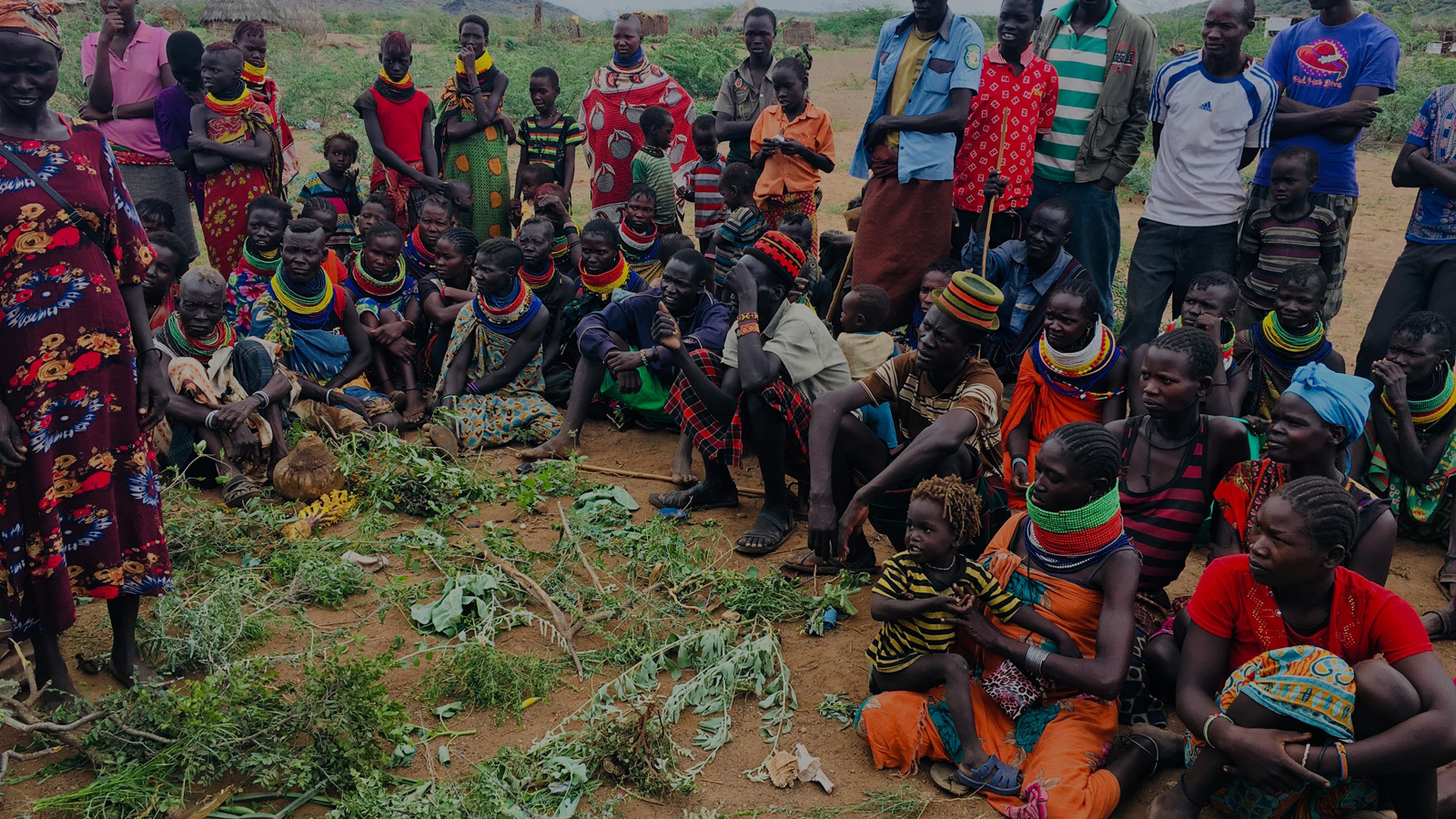 Group of Turkana community members sit around pile of plants