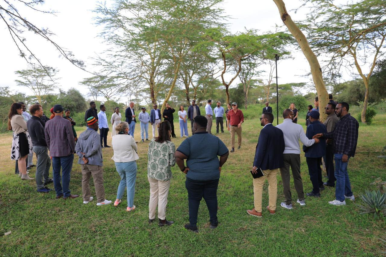 Group of people standing in a circle under acacia trees.